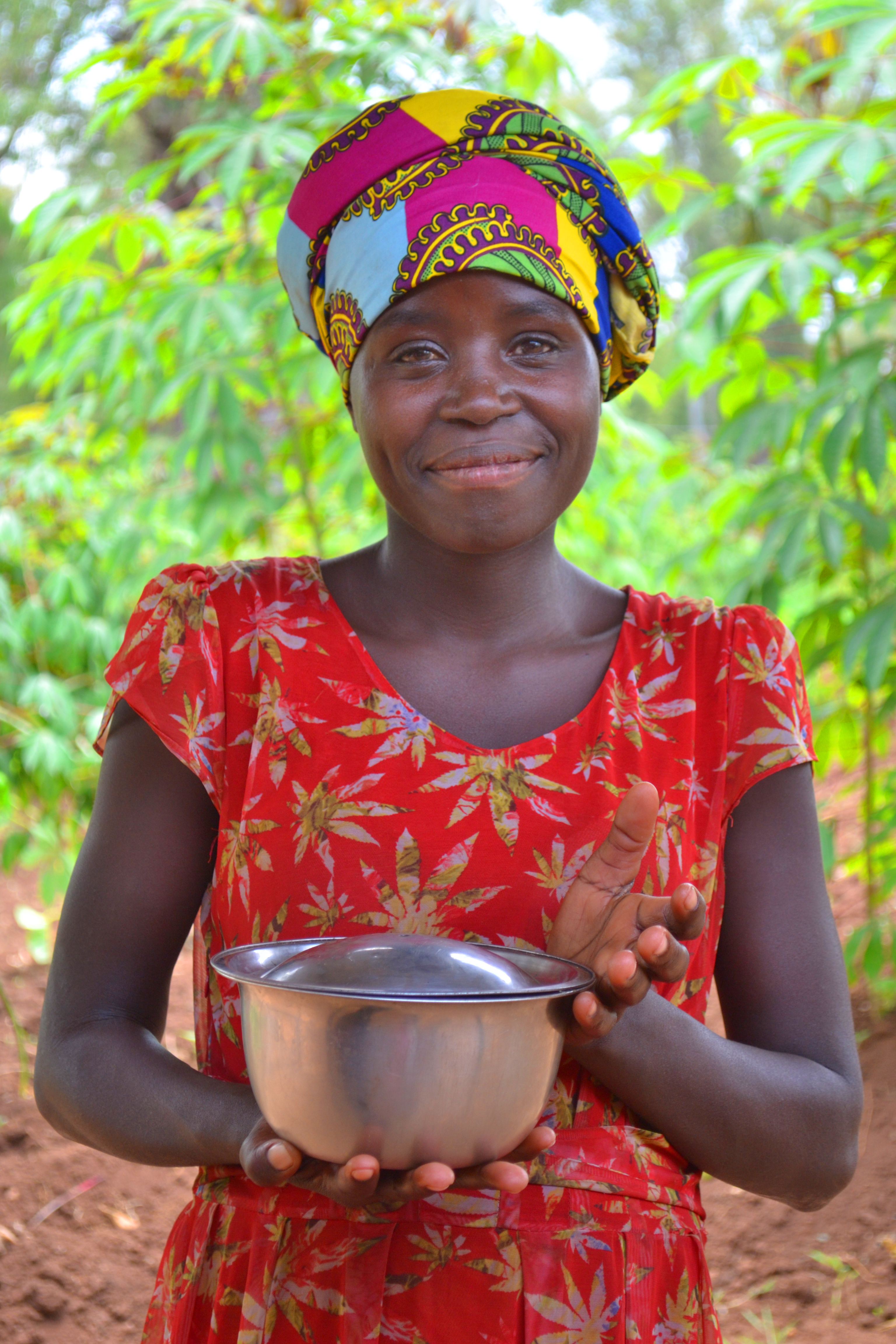 Woman holding pot wearing a red Kitenge dress and a multi-colored head wrap. 